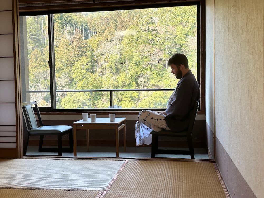 Foreign tourist wearing a yukata in a ryokan relaxing in his room in front of a window with view over the surrounding valley in Kyoto, Japan