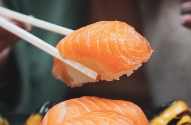 salmon sushi held between choptsicks