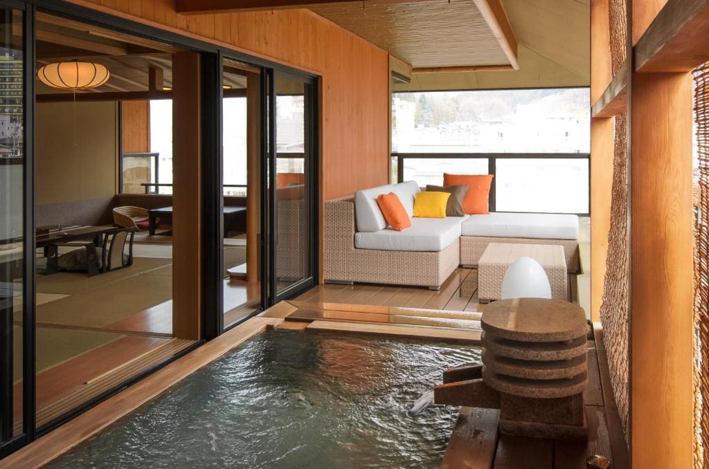 Private onsen bath on a wooden deck with wicker sofa seating, connected to a tatami room at Aburaya Tousen