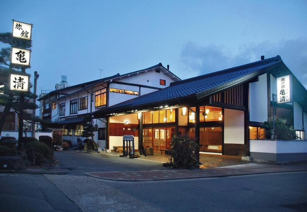 Exterior view of Kamesei Ryokan at dusk with lit entrance and traditional signage