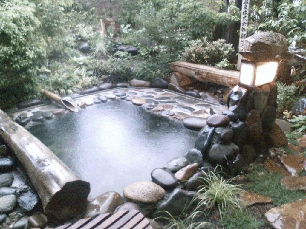 Private outdoor onsen bath surrounded by stones and garden plants at Kamesei Ryokan