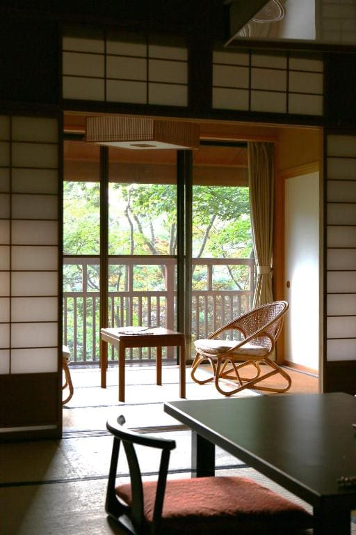 Tatami room with shoji screens, chairs, and balcony view at Kanbayashi Hotel Senjukaku
