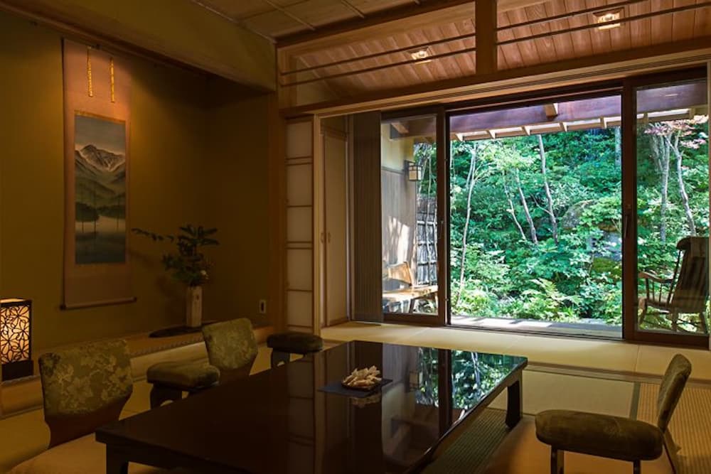 Tatami room with chairs and large window facing a forest at Seni Onsen Iwanoyu