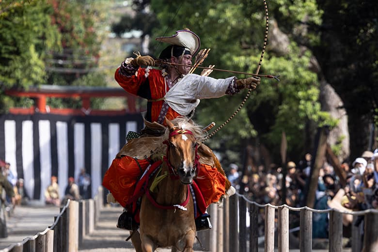 A yabusame archer in traditional samurai attire riding a galloping horse, skillfully aiming an arrow at a target during a ceremonial performance
