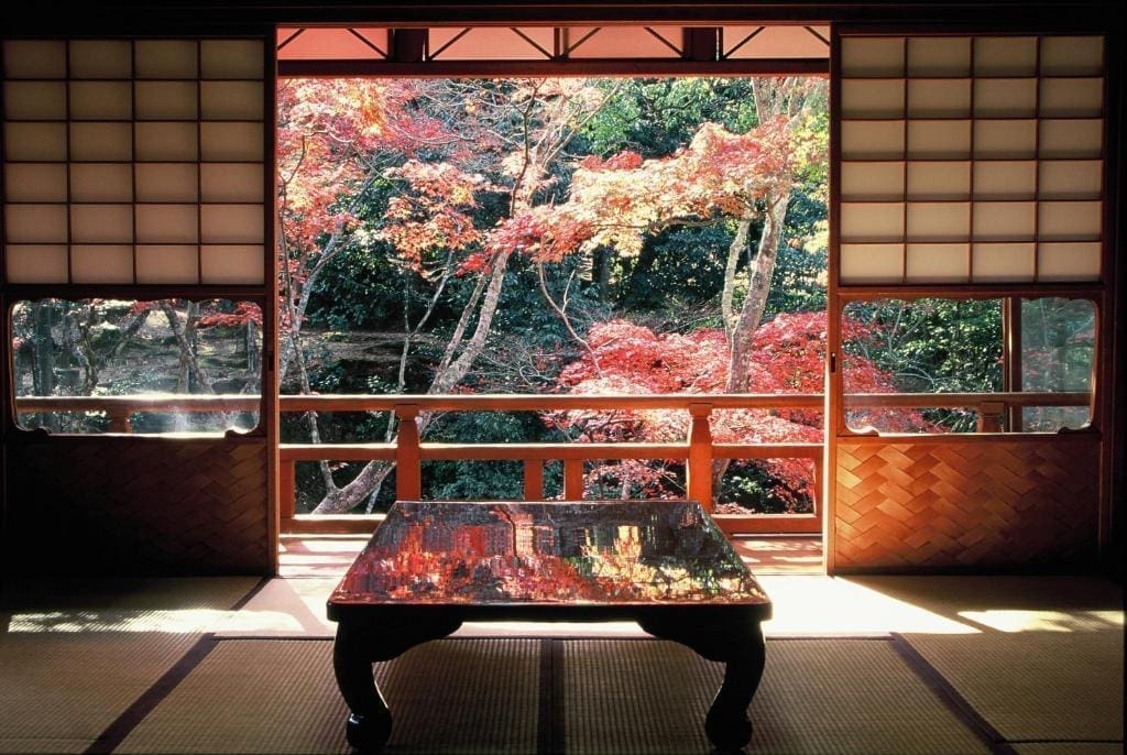 View from a tatami room at Iwaso looking out toward red autumn foliage through wooden balcony railings.