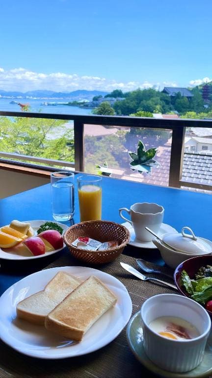 Western-style breakfast set with toast and juice on a blue table overlooking the sea and the torii gate in the distance.