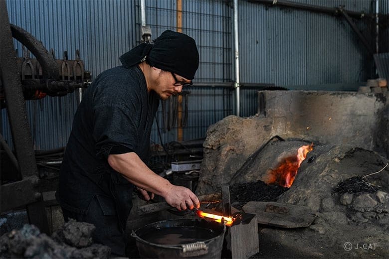 Japanese blacksmith working on a heated knife blade inside a forge during a traditional knife-making experience.