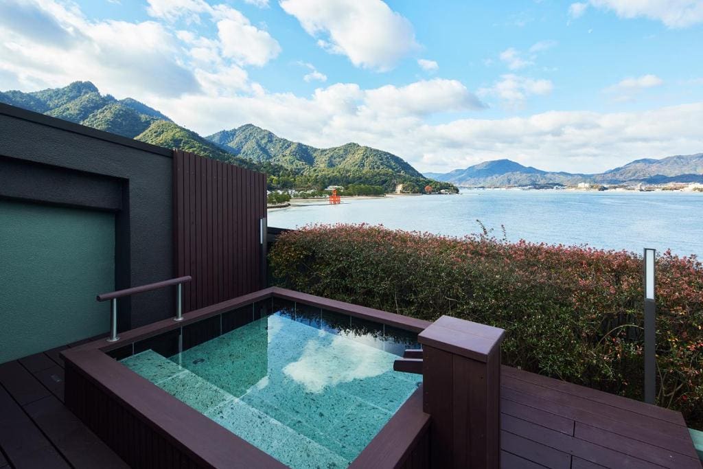 Outdoor rooftop bath at Kurayado Iroha with a view of the sea and surrounding mountains.