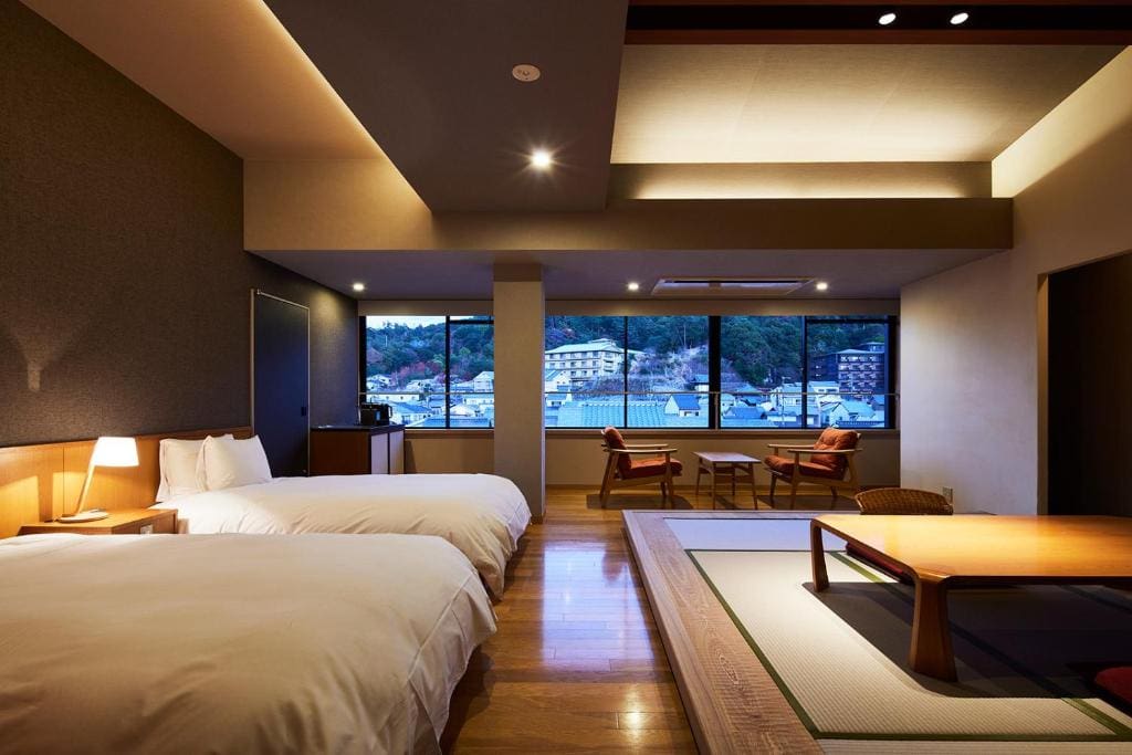 Spacious guest room at Kurayado Iroha with twin beds, a tatami seating area, and large windows overlooking the town.
