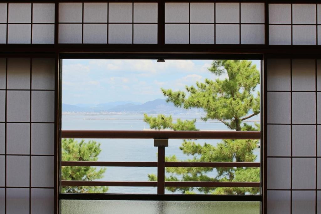 View of the ocean and pine trees seen through the window of a Japanese-style room at Miyajima Seaside Hotel.