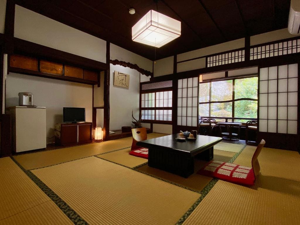 Traditional tatami room at Ryoso Kawaguchi with low table, zabuton cushions, and a view of trees through the window.