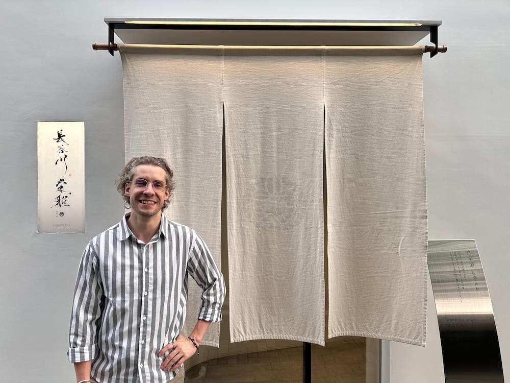 Person standing in front of the white entrance curtain at Hasegawa Eiga sake tasting venue in Tokyo.