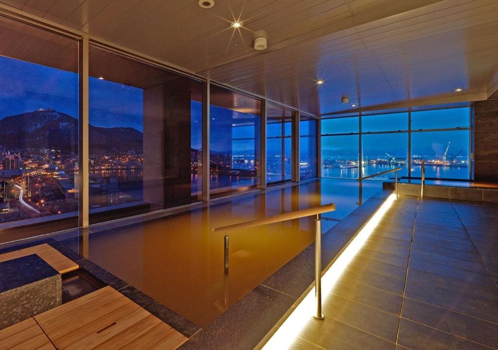Indoor onsen pool at Century Marina Hakodate with panoramic night view of Hakodate city and harbor