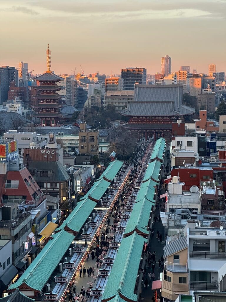 Crowds walking along the green-roofed Nakamise shopping street leading to the five-story pagoda and main hall of Sensō-ji temple in Asakusa, Tokyo at sunset
