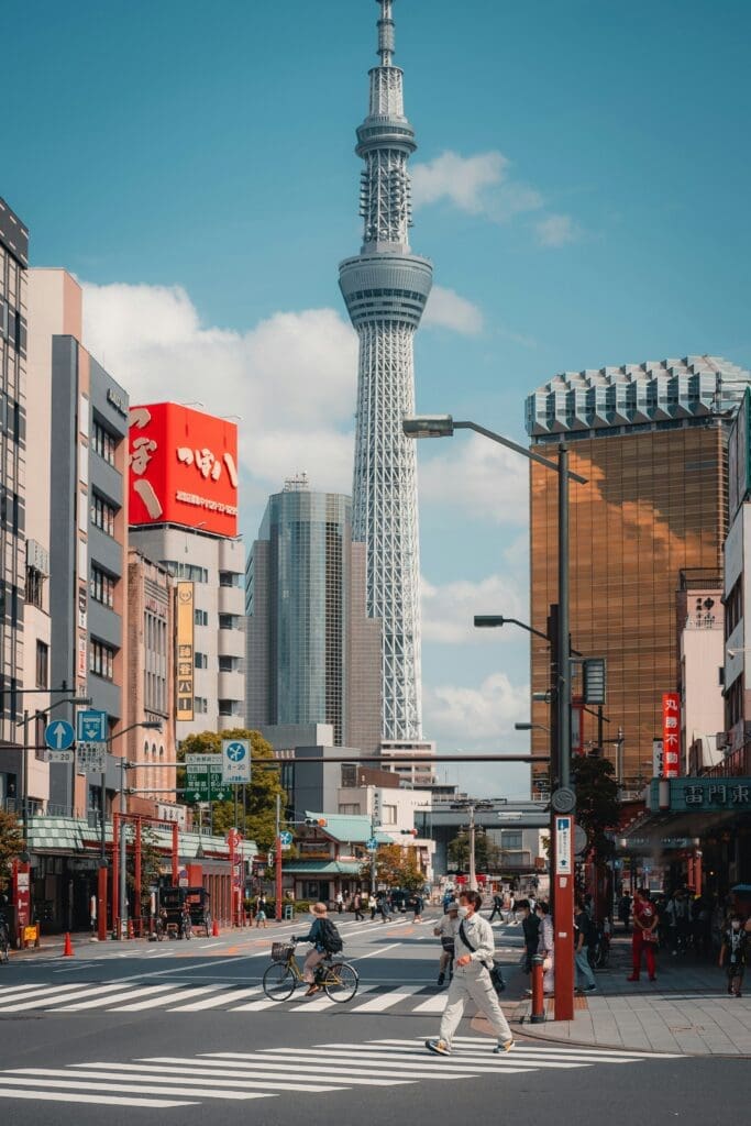 People crossing a street in Asakusa, Tokyo, with Tokyo Skytree tower visible against a blue sky