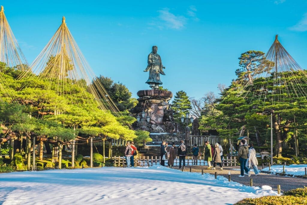 Visitors admire a stone statue amid snow and yukitsuri-supported pines in Kenrokuen Garden, Kanazawa