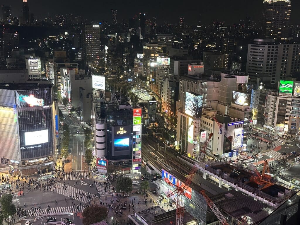 Aerial view of Shibuya scramble crossing from Ce La Vi, with illuminated billboards, train tracks and construction cranes at night in Tokyo