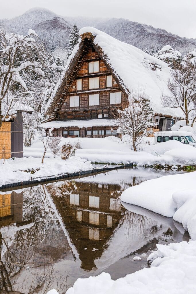 Thatched gassho-zukuri house in Shirakawa-go covered in snow reflected in a pond