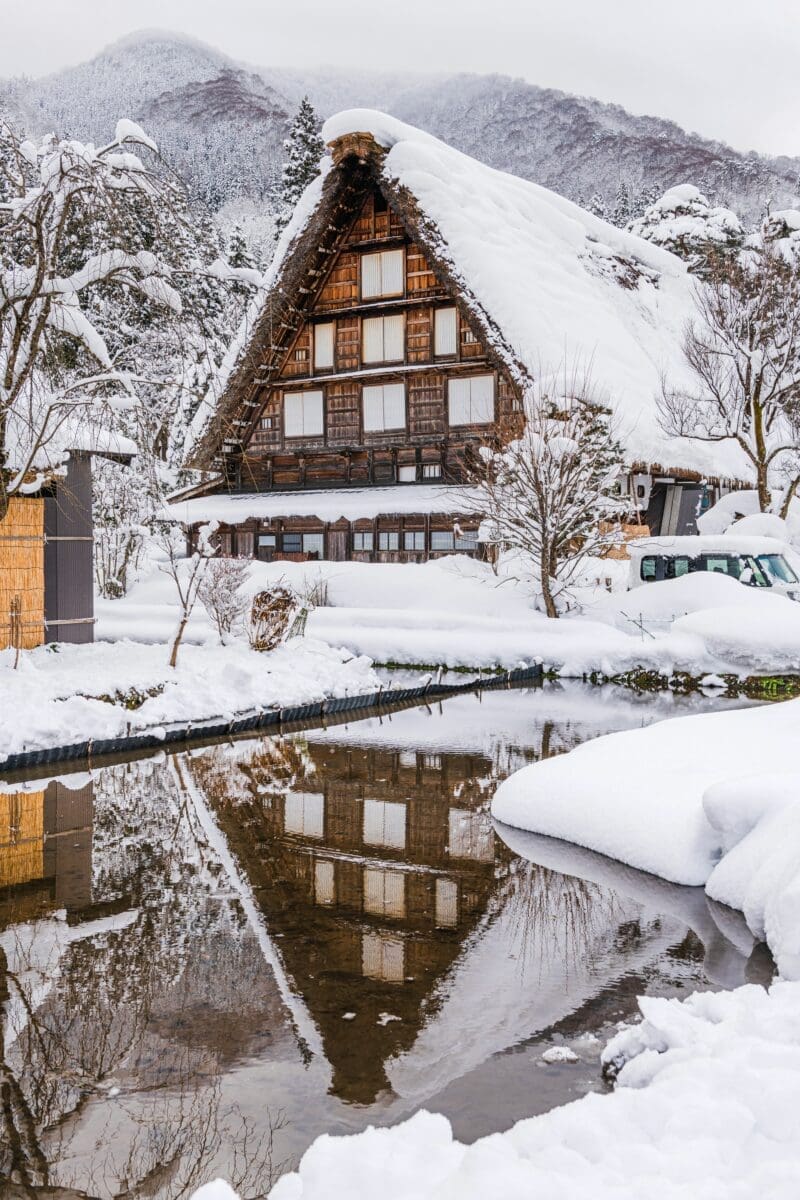 Snow-covered gassho-zukuri farmhouse reflected in water in Shirakawa-go