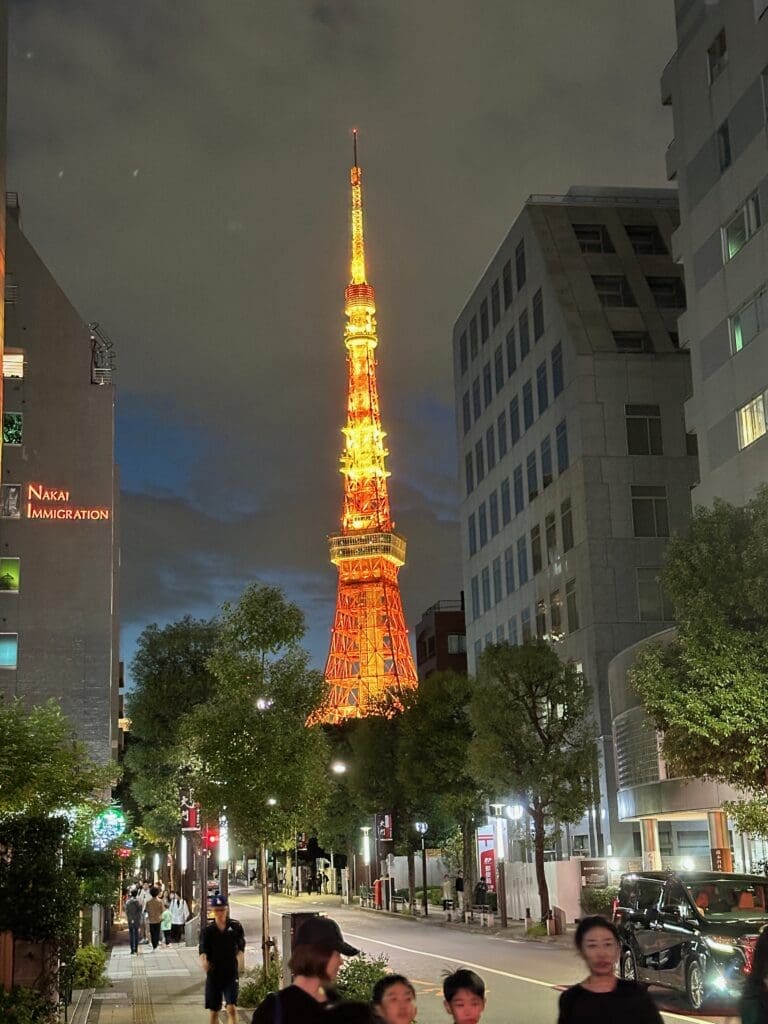 Tokyo Tower lit up at night behind a city street with buildings and pedestrians