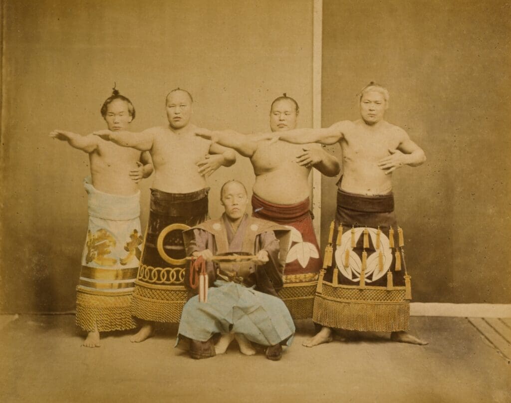Four Japanese sumo wrestlers in ceremonial aprons and a kneeling sumo referee