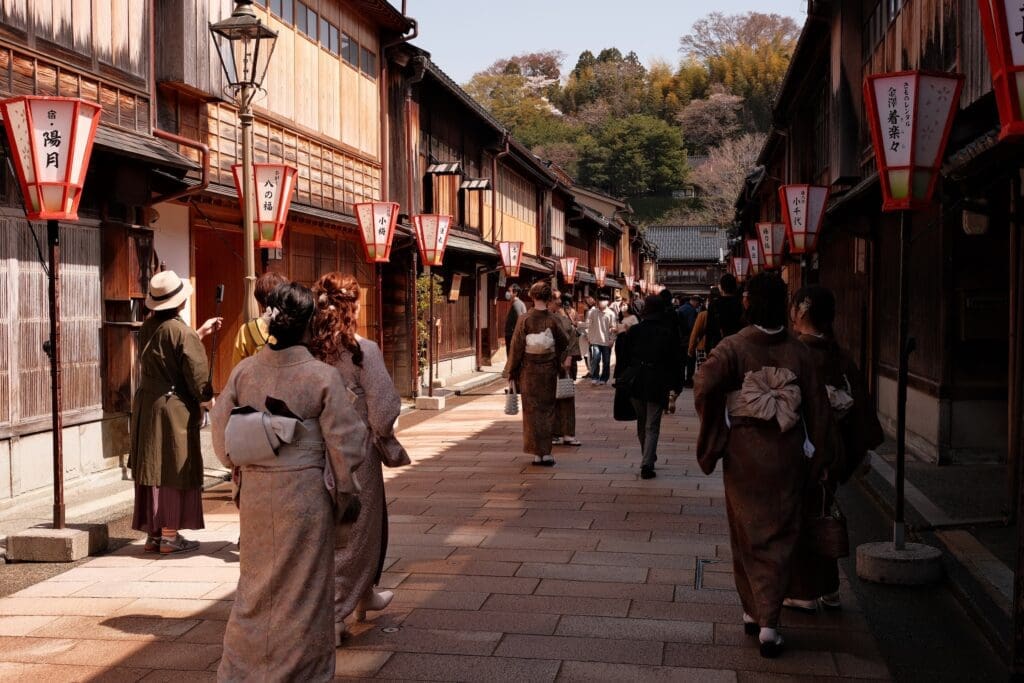Visitors in kimonos walking along stone-paved Kanazawa Higashi Chaya Street with wooden tea houses and red lanterns
