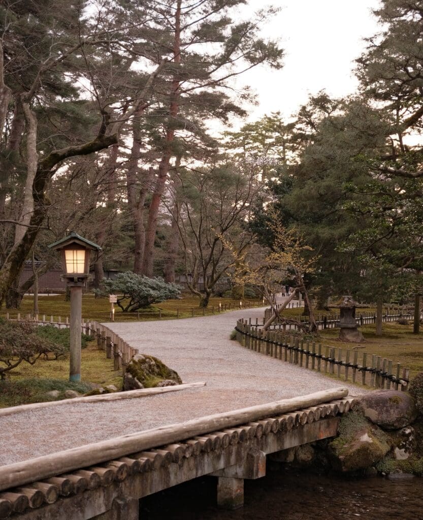 wooden footbridge over stream in Kenrokuen Garden with lantern and trees