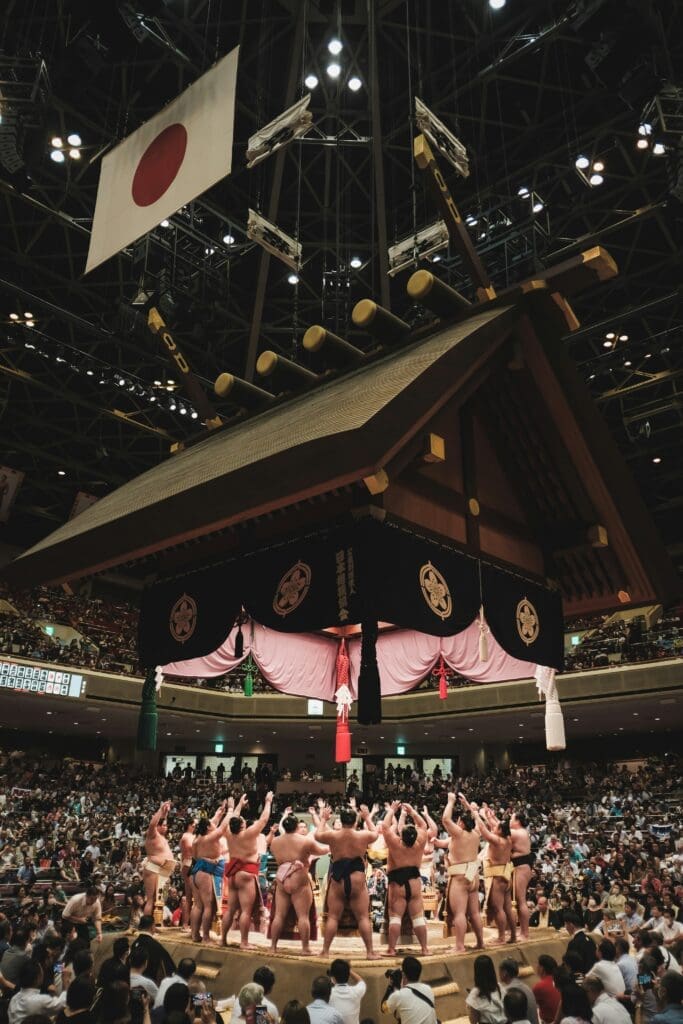 Sumo wrestlers in ring entering ceremony under ceremonial roof and Japanese flag at Ryogoku Kokugikan