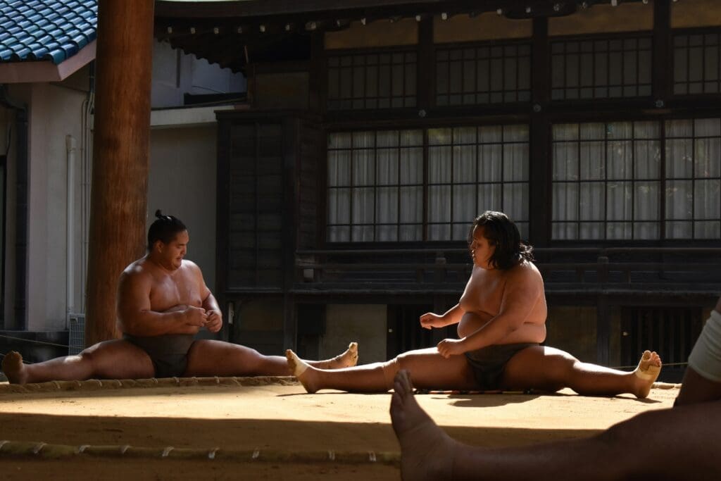 Two sumo wrestlers stretching splits in a Japanese training stable