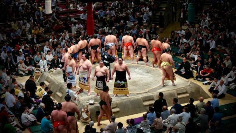 sumo wrestlers standing in a dohyo ring at Tokyo Kokugikan with spectators around
