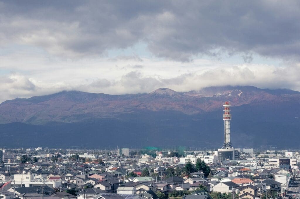 Mount Azuma-kofuji viewed from Sakuramoto, Fukushima, with city rooftops and a red-and-white communication tower under a cloudy sky