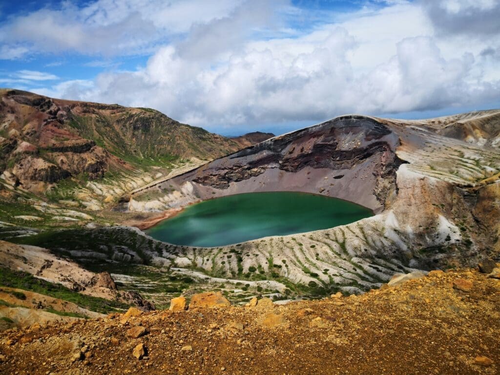 Okama crater lake on Mount Zaō near Zao Onsen in Yamagata, Japan, turquoise water in a volcanic caldera under partly cloudy sky