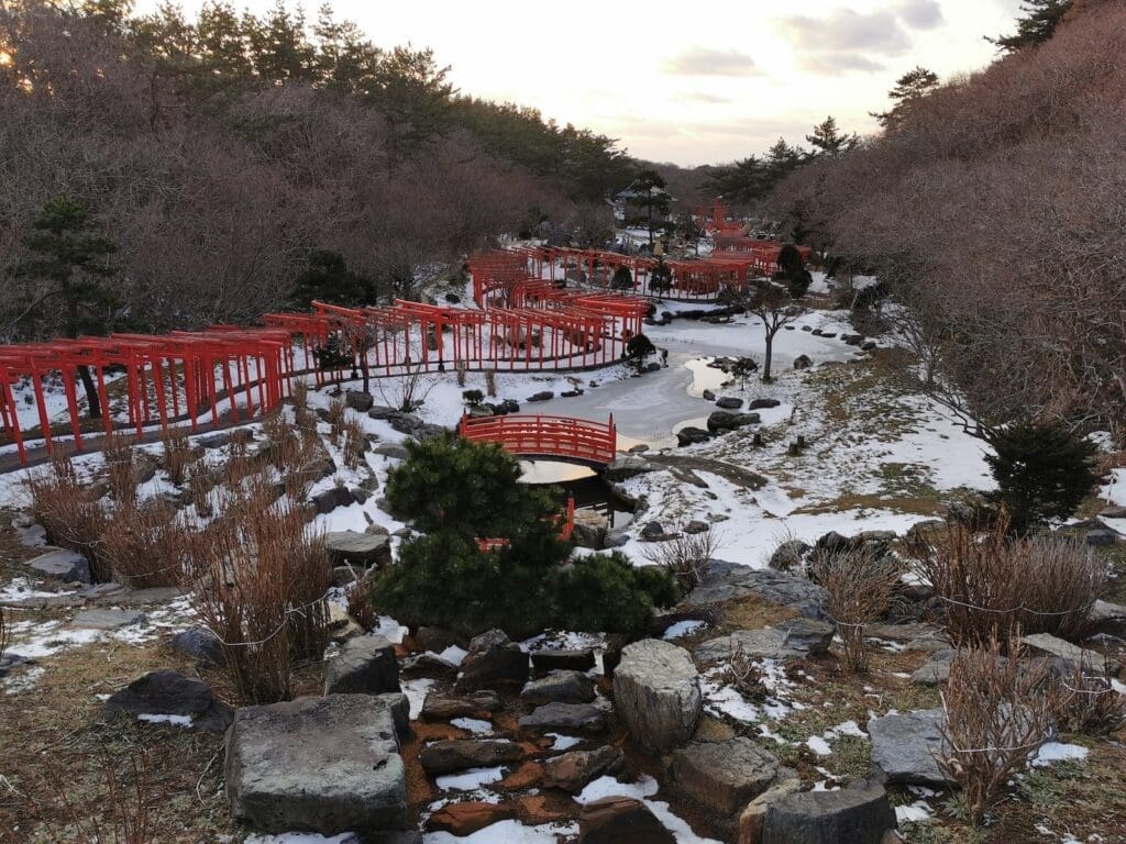 Takayama Inari Shrine in winter with red torii gates and bridges over a partially frozen stream in Tsugaru, Aomori, Japan