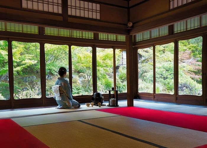 Tea ceremony at Sakaguchian teahouse, woman in kimono kneeling on tatami with windows opening to a lush Japanese garden